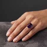 A model's hand wearing the London Bridge ring with a rectangular fancy purple sapphire set in a gold band.